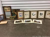 Overall grouping of small framed and unframed art arranged on floor against a storage unit.