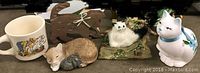 Coffee cup and four cat figurines including wooden, resin, and plush types