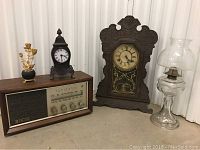 Photo showing all items in the lot: two clocks, the AM/FM radio, oil lamp, and metal roses in vase.