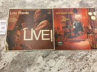 Two vinyl record albums featuring Lou Rawls and Nat King Cole displayed side by side on a granite countertop; visible wear on covers.