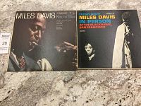 Two vinyl records side by side: 'Kind of Blue' and 'In Person at the Blackhawk, San Francisco' by Miles Davis on a stone surface.