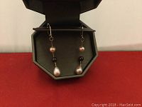 Close-up of the pair of unevenly colored freshwater cultured pearl dangle earrings with latch back hooks inside the box