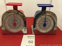 Two Taylor mechanical kitchen scales side by side, red and blue with glass front on red and missing glass on blue.