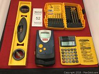 Photo showing all items in the lot: yellow plastic level, Ryobi device, yellow calculator, and a yellow case with drill and screwdriver bits.