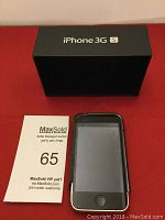 Front view of black iPhone 3GS with original box behind it on a red surface, showing phone screen and home button.