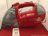 Red Bissell Spotlifter 2X handheld wet vacuum cleaner, showing full side profile with handle and transparent fluid containers.