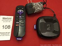 Roku 2 streaming player with remote control and power adapter on a red surface.