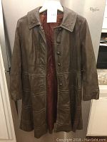 Front view of a brown women's leather jacket hanging on a hanger, showing buttons and inner lining.