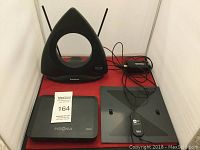 Photo showing two HD antennas (RadioShack triangular and flat square antenna) and the Insignia electronic box on a red surface.