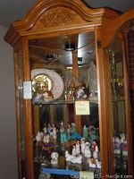 Wooden glass cabinet containing various glass, ceramic, and stone religious and Christmas figurines forming nativity scenes