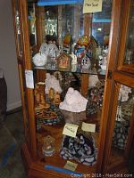 Full view of three shelves inside wooden curio cabinet with religious figurines and nativity scenes displayed.