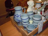 Wide view of lot showing stoneware pieces, bust, figurines and floral pitcher in cardboard box