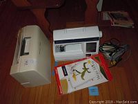 Sewing machine next to carrying case, Mega Hoop box and cords