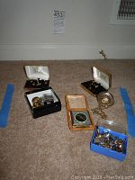 Lot items on carpet showing Franklin Mint Eagle pocket watch with attached chain, vintage travel alarm clock in tan leather case, multiple cuff links, and tie pins in boxes and bags.
