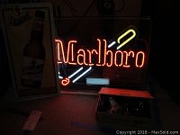 Lit Marlboro neon sign, Leinenkugel beer sign, and box with bottle openers visible on floor