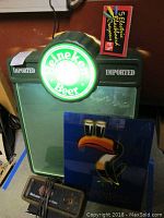 Heineken illuminated blackboard light with ‘Imported’ moldings, green display panel, box of five electric chalk markers on top, Guinness glass poster leaning in front, Miller clock sign at bottom