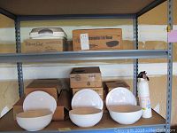 Shelf view showing boxed Pampered Chef rectangular lid/bowl server and three round white bowls with lids, along with additional boxes.