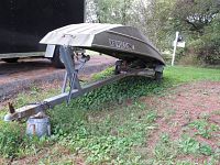 Boat trailer upside down with visible galvanized frame, support brackets, and rust on hitch area.