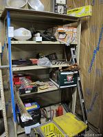 Metal shelving unit with various tools and boxed items arranged on shelves, including a yellow ladder and black toolboxes.