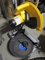 Side view of DeWalt 14 inch chop saw showing yellow motor housing, yellow blade guard, gray metal base, and round cutting table with clamping mechanism.