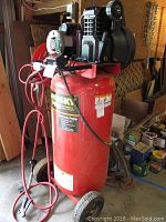 Front view of red vertical tank, two wheels, attached hose