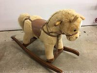 Full view of plush rocking horse showing light beige body, wooden rockers, and leather saddle.