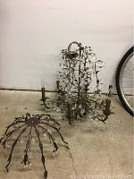 Photo showing both the chandelier and the matching decorative light figure on a concrete floor. The chandelier has multiple candle style bulbs with crystal-like drops on metal branches.