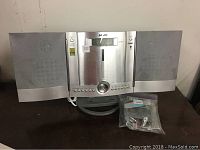 Front view of Sanyo stereo system showing pop-out CD player, speakers, control buttons, and remote control in plastic bag.