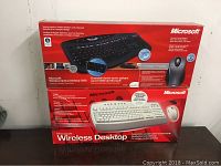 Two boxed Microsoft wireless desktop sets stacked; one black keyboard set and one white keyboard set, in original packaging showing model names and branding.