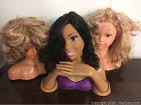 Three hair mannequin busts displayed together showing distinct hair styles and signs of wear.