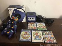 Overall shot of indigo GameCube console, original box, three controllers, five game cases and cables.
