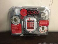 Front view of the Sudoku handheld game in sealed clear plastic packaging showing brand name, illuminated mega screen, and styling.