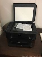 Canon Pixma MG3520 printer with top lid open showing scanner glass, installation disc and manual on the scanner bed.