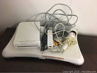 Nintendo Wii console, remote, nunchuk, power and AV cables, and balance board on a flat surface.