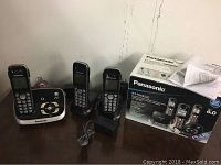 Expandable cordless phone set with three handsets displayed alongside power adapter and original box on table.