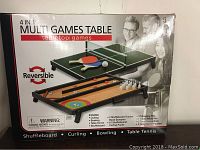 Photo of the boxed 4 in 1 multi games table showing reversible sides for table tennis and shuffleboard with bowling pins and accessories.