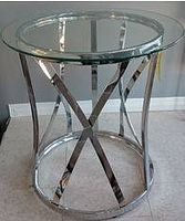 Front angle view of the chrome and glass table showing round glass top and shiny chrome crossed supports base.