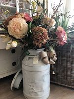 Full view of silk flower bouquet in white distressed metal milk jug with decorative bow