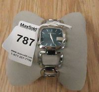 Front view of watch on cushion showing square case, green dial and link bracelet with lot tag