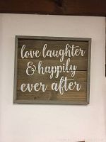 Wooden wall sign with text 'love laughter & happily ever after' in white cursive on rustic wood background with gray frame.