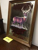 Framed Miller High Life mirror sign with a deer image shown from an angle. Visible wear and scratches on mirror surface.