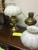 Two vintage brass lamps on a wooden table, one with milk glass shade attached, the other with shade removed showing converted oil lamp burner