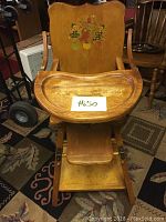 Front view of vintage wooden high chair with a tray attached and painted designs on the backrest and seat area.
