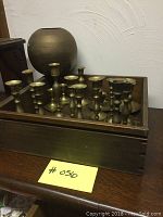 Full view of all brass candle sticks and spherical vase positioned within the wooden box.