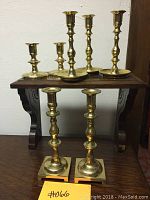 Eight brass candle sticks on display showing three different height groups: one pair 10 inches tall, two pairs about 7 inches tall on a wood shelf, and a smaller pair on the lower surface.