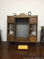 Full view of wooden hanging shelf showing four drawers, four cubbies, and wire mesh backing with metal hanging rings