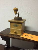 Side view of the wooden base and metal top of the KYM coffee grinder showing the crank handle and small drawer