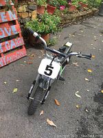 Front view of Razor MX350 electric child bike with knobby tires, number 5 on front plate, situated on pavement with plants in background.