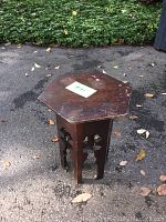 Full view of the wooden hexagonal side table on outdoor pavement, showing the top and legs.