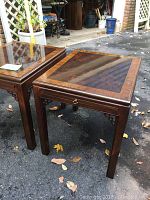 Two Drexel Heritage wood side tables with glass inset tops placed outside on a driveway showing front and top views